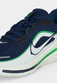 Μπλε ναυτικό αθλητικό παπούτσι Nike με λευκές και πράσινες λεπτομέρειες, μαξιλαρωμένη σόλα και πλέγμα πάνω μέρος με μαύρο σχέδιο κορδονιών σε ζιγκ-ζαγκ.