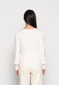 Lichtroze pullover trui met een ronde halslijn en pofmouwen, gemaakt van een zachte stof, gecombineerd met crèmekleurige broeken.