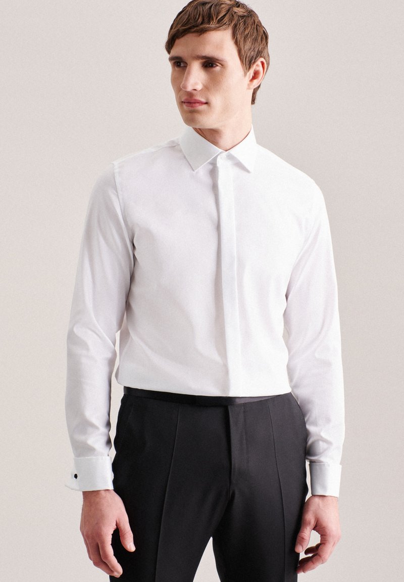 Chemise blanche à manches longues en coton, avec un col classique, une patte de boutonnage à l'avant, des poignets boutonnés avec des accents noirs, associée à un pantalon noir.