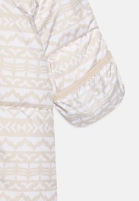 Manche de doudoune beige avec des motifs géométriques blancs, présentant une texture froncée et des accents en tissu lisse contrastants.