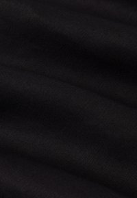 Tessuto nero con una superficie liscia, che mostra sottili motivi intrecciati. Il materiale appare leggero, drappeggiandosi elegantemente in pieghe.