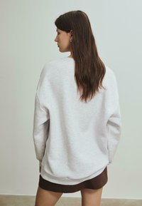 Lys grå oversized sweatshirt med en blød tekstur, rund halsudskæring og dropped shoulder, parret med en mørkebrun nederdel.