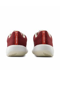 Scarpe da ginnastica rosse con una parte superiore in rete testurizzata, suole bianche e un marchio prominente sul tallone. Presentano una punta arrotondata e un design imbottito.