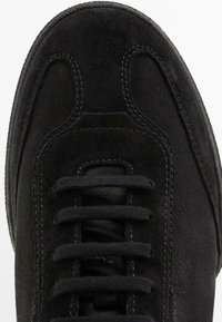 Sneaker in suede nero con punta arrotondata, lacci piatti neri e cuciture a contrasto. Texture liscia e design minimalista.