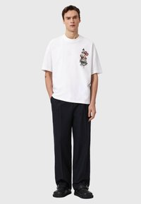 Λευκό βαμβακερό t-shirt με κοντά μανίκια, διακοσμημένο με πολύχρωμο κεντητό σχέδιο στο αριστερό στήθος. Συνδυασμένο με μαύρο, άνετο παντελόνι.