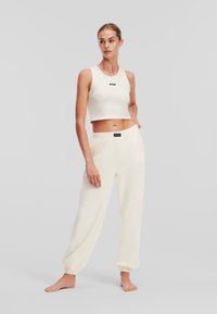 Kermanvärinen puuvillainen crop-top ja yhteensopivat rento-malliset joggerit, joissa on elastiset hihansuut. Päällä on pieni musta logo topissa ja vyötäröllä.