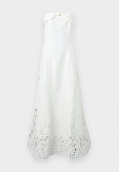 Λευκό φόρεμα χωρίς τιράντες με κόμπο στη λαιμόκοψη, εφαρμοστή μπλούζα και μπροκάρ δαντέλα με λουλουδάτα μοτίβα κατά μήκος του τελειώματος, που επεκτείνεται προς τα πάνω στις πλευρές.