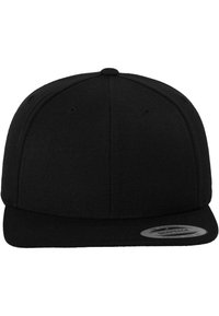 Casquette snapback noire en tissu texturé, avec une visière plate, un design structuré à six panneaux, et un patch rond avec logo sur le côté gauche.