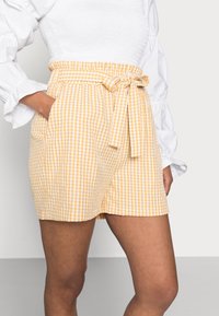 Žluté kostkované šortky s elastickým pasem a zavázacím páskem. Vyrobené z lehké látky, mají dvě boční kapsy.