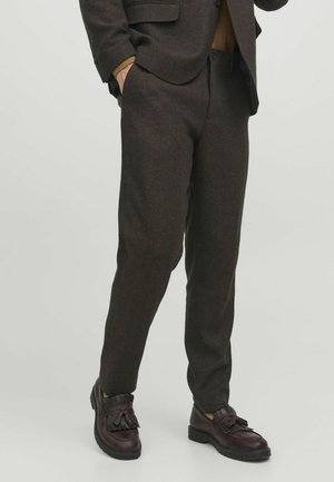 Braune Tweed-Hosen mit strukturiertem Muster, im Slim-Fit-Schnitt und seitlichen Taschen, kombiniert mit dunklen Lederschuhen mit dekorativem Fransen.