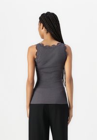 Canottiera grigia a coste con un design aderente e pizzo lungo le spalle, abbinata a pantaloni neri a vita alta.