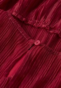 Nahaufnahme eines roten, plissierten Stoffs mit einem kleinen roten Knopf, der durch eine Schlaufe befestigt ist.