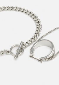 Silbernes Schmuckset mit einer groben Kettenhalskette mit einem Toggle-Verschluss und einem runden Creolenohrring. Glatte, glänzende Metalloberfläche.