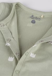 Body in cotone verde chiaro con scollo rotondo, motivi di corone bianche e bottoni automatici lungo la patta frontale per facilitare la vestizione.