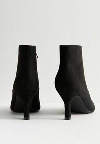 Stivaletti neri in suede, con punta rotonda, tacco medio e zip laterale. Texture liscia e design semplice.