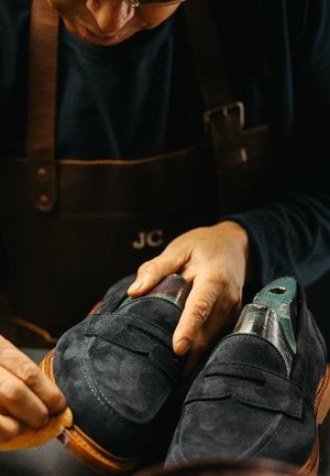 Donkerblauwe suède schoenen met een gestructureerd oppervlak, voorzien van leren zolen in bruin en een unieke groene en gemusterde accent op de bovenkant.