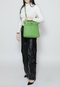 Groene leren tas met een gestructureerd ontwerp, gerolde bovenkant en metalen hardware accenten. Beschikt over een gladde textuur en een verstelbare schouderriem.