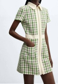 Vestito a quadri verdi e bianchi con zip frontale, maniche corte e tasche laterali. Il tessuto ha una finitura strutturata con colletto.