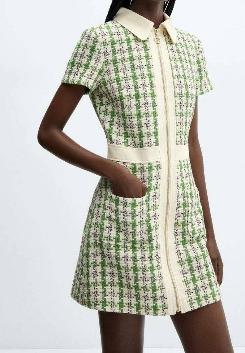 Vestito a quadri verdi e bianchi con zip frontale, maniche corte e tasche laterali. Il tessuto ha una finitura strutturata con colletto.
