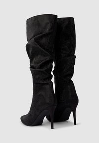 Czarne botki na wysokim obcasie wykonane z teksturowanego materiału, charakteryzujące się luźnym fasonem, zdobione dżetami i spiczastym czubkiem.