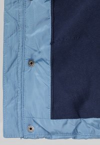 Lichtblauwe gequiltede stof met een marineblauwe fleece binnenkant. Voorzien van drukknoophardware en zichtbare stikselranden. Zachte, gestructureerde oppervlakte.