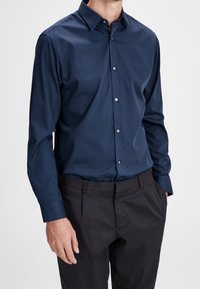 Granatowa koszula zapinana na guziki, wykonana z gładkiej tkaniny, z ostrym kołnierzykiem i długimi rękawami, zestawiona z czarnymi eleganckimi spodniami. Posiada guziki z przodu.