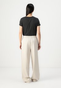 Black short-sleeve t-shirt paired with light beige wide-leg trousers featuring an elastic waistband and two back pockets.