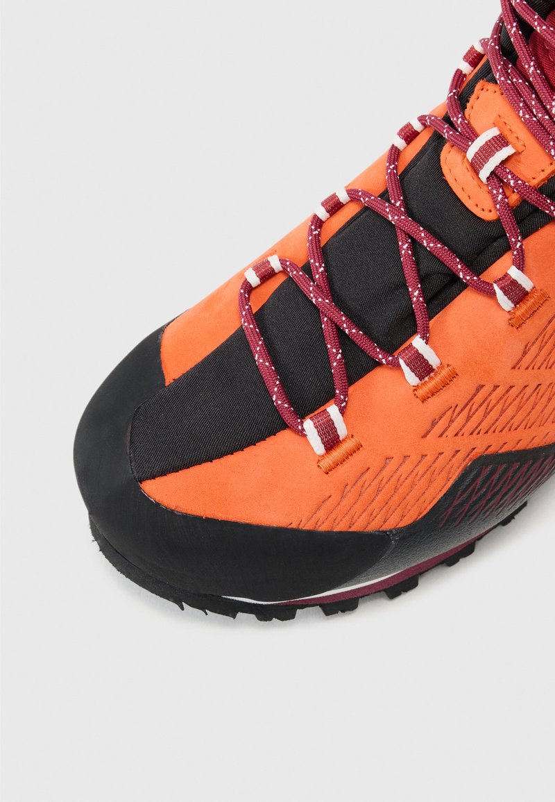 Zapatilla de senderismo naranja y negra con materiales de ante texturizado, malla y goma. Presenta cordones color burdeos y patrones diagonales distintivos en el costado.