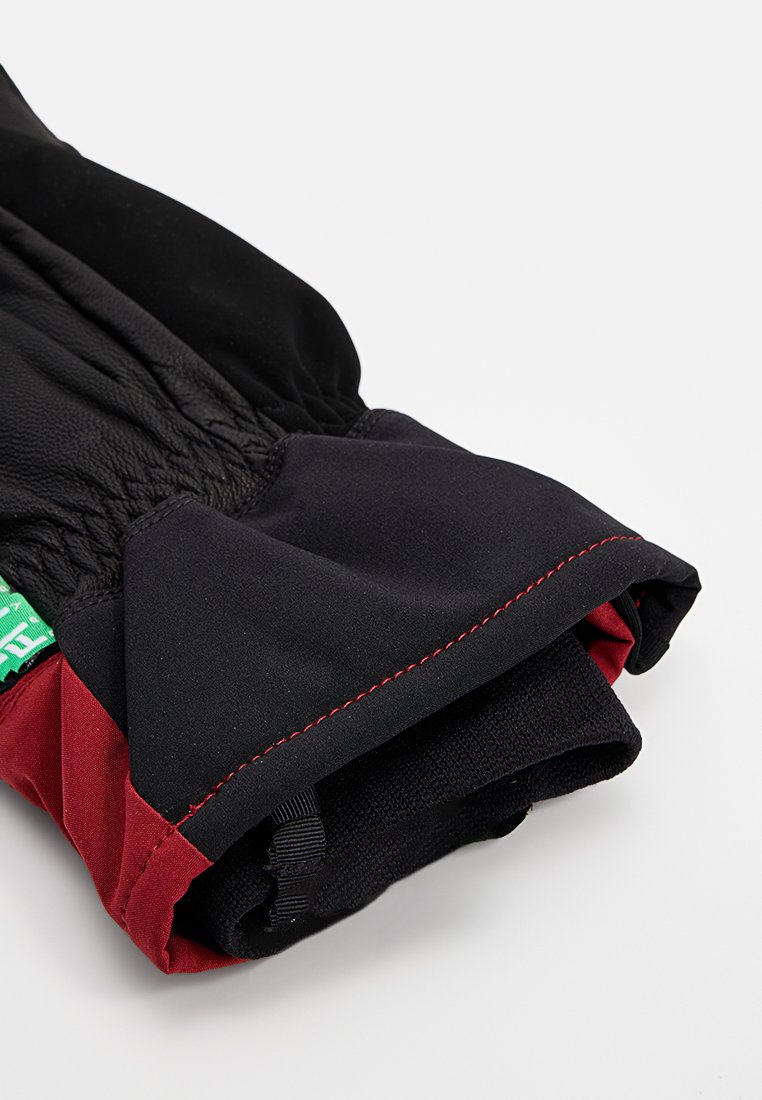 Zwarte en rode winterhandschoen met leren bovenkant, elastische pols en rode stiksels. Voorzien van een groen label dat aan de zijkant is gestikt.