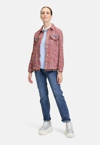 Rood en roze tweed jasje met rafelige randen, twee voorzakken, gedragen over een lichtblauw overhemd met knopen en gecombineerd met blauw gespetterde jeans.