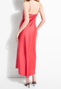 Rode satijnen maxi-jurk met dunne bandjes, vloeiende ontwerp, afgeronde zoom en een gladde textuur. Draag het met zwarte hoge hakken.