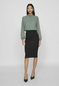 Zielona bluzka w wzory z bufkami, zestawiona z dopasowaną czarną spódnicą ołówkową, charakteryzującą się gładką fakturą i długością do kolan.