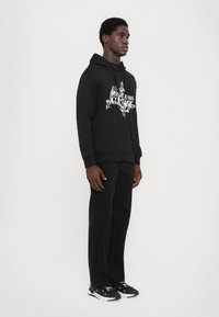 Sweatshirt preto com design gráfico na frente, em material de algodão, com punhos ajustados, combinado com calças pretas de perna reta e sapatilhas desportivas pretas.