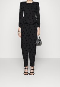 Černý komplet s texturovaným vrchním dílem s peplum a zúženými kalhotami s abstraktními vzory. Doplněno černými páskovými sandály a mini kabelkou.