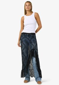 Džínové kalhoty s černou vrstvou krajky. Krajka má květinové vzory a volánkový lem, což vytváří výrazný dvouvrstvý efekt.