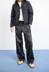 Czarna pikowana kurtka z kapturem, noszona na białej koszuli. Luźne czarne spodnie typu cargo z kieszeniami, uzupełnione �żółtymi trampkami.