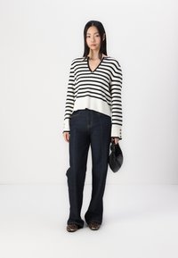 Striped black and white V-neck sweater, dark blue high-waisted jeans, black clutch bag, and animal print shoes, standing against a white background.
