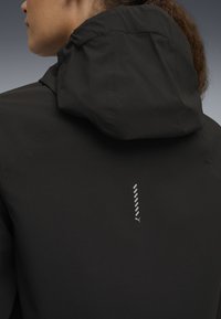 Veste à capuche noire avec une texture lisse, arborant un design vertical réfléchissant et un logo près du cou. Design minimaliste et épuré.