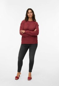 Pull en tricot rouge avec des accents floraux sur les épaules, associé à un jean skinny noir et des sandales à talons rouges avec un détail en nœud.