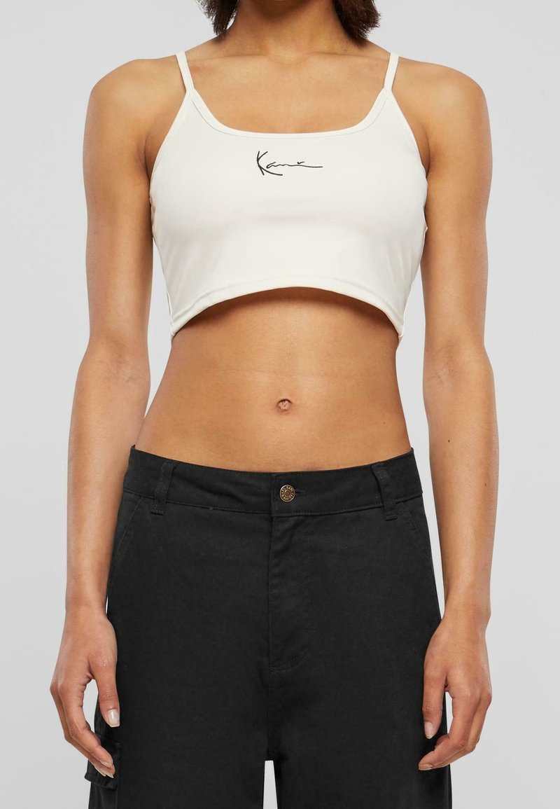 Top de tank court blanc avec de fines bretelles et un logo en script noir. Assorti à un pantalon noir taille haute avec un détail de bouton.