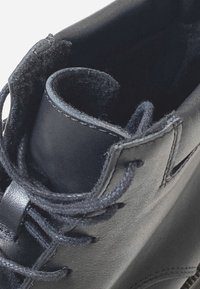 Stivale in pelle nera con finitura testurizzata, caratterizzato da lacci neri e un'apertura superiore liscia e senza cuciture. Gli elementi di design includono cuciture a vista.