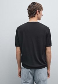 Černá krátká rukávová košile vyrobená z měkké tkaniny, má žebrovaný výstřih a volný střih, kombinovaná s světle modrými džíny.