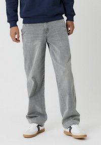 Hellgraue, gerade geschnittene Jeans aus Denim, mit einer dezenten Textur und sichtbaren Nähten. Kombiniert mit weißen Turnschuhen und einem marineblauen Sweatshirt.