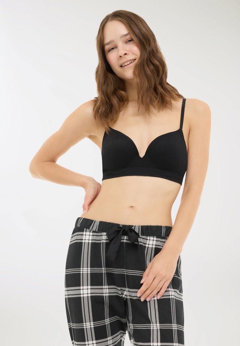 Reggiseno wireless nero con scollatura profonda, abbinato a pantaloni del pigiama a scacchi bianchi e neri con vita elastica e lacci.