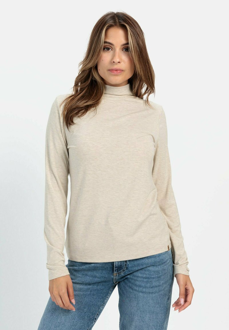 Beige Langarm-Turtleneck-Hemd aus weichem Material, mit einem figurnahen Design und einer dezenten Struktur. Kombiniert mit blauen Jeans.