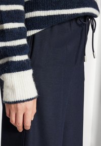 Stickad marinblå och vit randig tröja med en texturerad tyg; åtsittande ärmslut. Mörk marinblå byxor med dragsko.