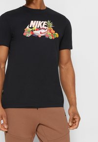 Svart bomullströja med korta ärmar som har en färgglad fruktgrafik och ordet "NIKE" i rosa. Normal passform och rund halsringning.