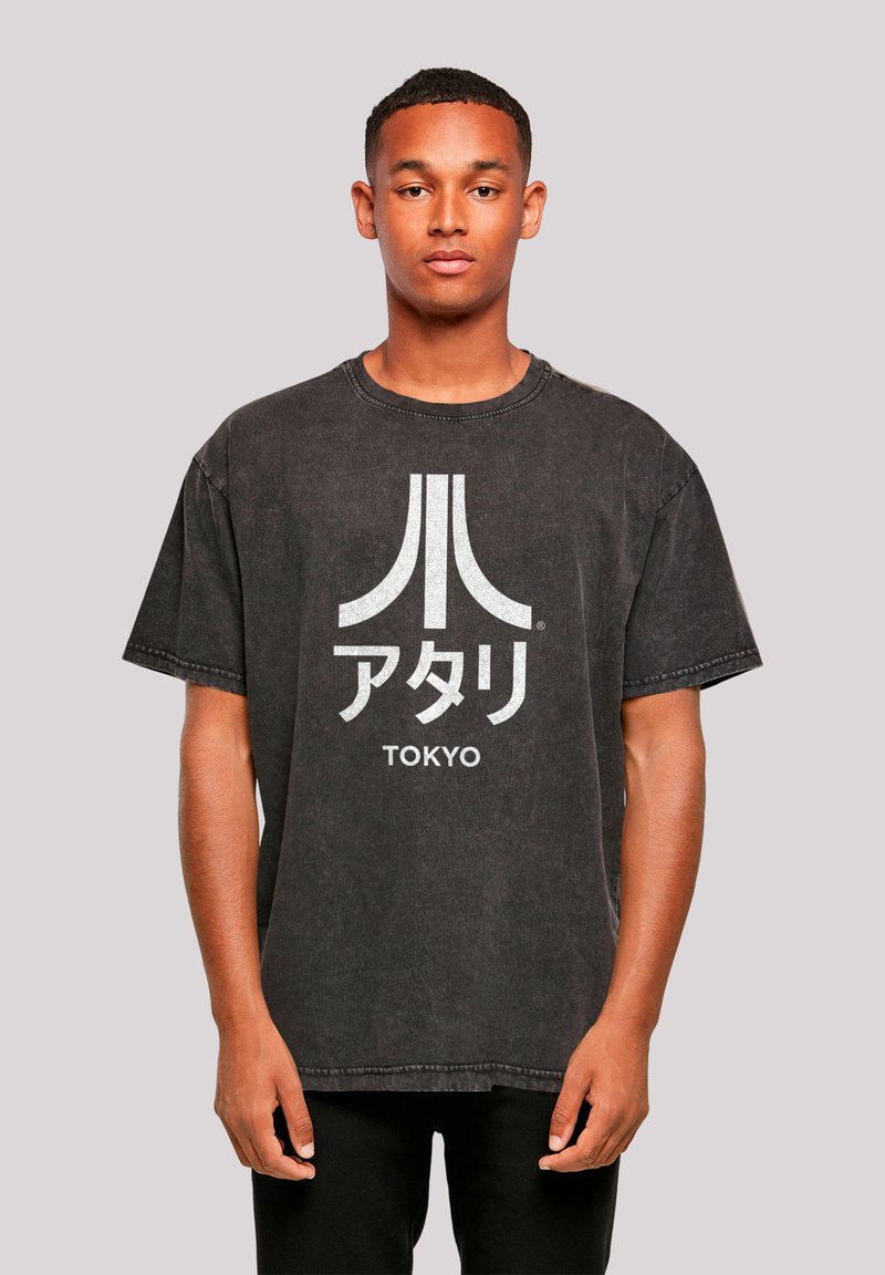 Schwarzes Oversized-T-Shirt aus Baumwolle, mit einem auffälligen weißen Atari-Logo und dem japanischen Text "TOKYO", der auf der Vorderseite aufgedruckt ist.