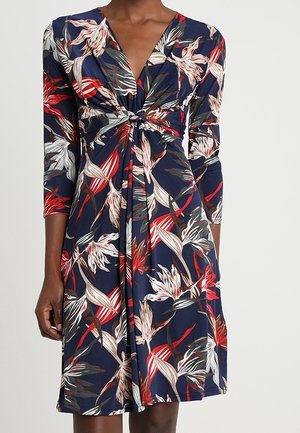 Granatowa sukienka do kolan z czerwonym, białym i beżowym kwiatowym wzorem, rękawami do łokcia oraz skręconym węzłem z przodu.
