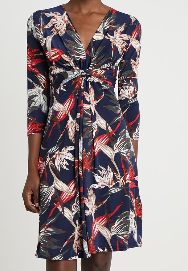 Robe bleu marine longueur genou avec motif floral rouge, blanc et beige, manches trois-quarts, et détail de nœud torsadé à l'avant.